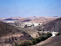 Das Foto zeigt den Blick vom Wadi Ghwair in das Wadi Faynan und auf den byzantinischen Siedlungshügel, mit den angrenzenden Verhüttungsplätzen (grauschwarz).