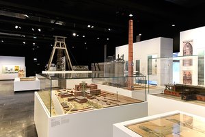 Blick in eine Ausstellungshalle des Deutschen Bergbau-Museums Bochum. Im Vordergrund ein Modell der Zeche Germania, im Hintergrund ein großes Modell des Förderturms der Zeche Germania.