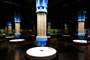 Blick in einen Ausstellungsraum im Rundgang Steinkohle. In der Mitte steht eine angeleuchtete Tauchpumpe für Grubenwasser, die durch Glasinstallationen unendlich gespiegelt werden.