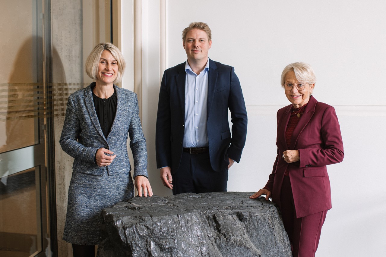 Drei Personen stehen vor dekorativem Kohleblock